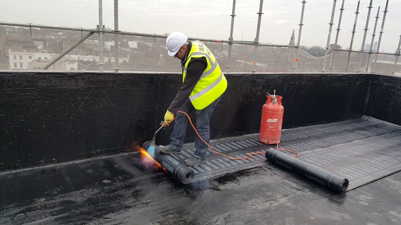 Worker applying sheet on roof to control waterproofing